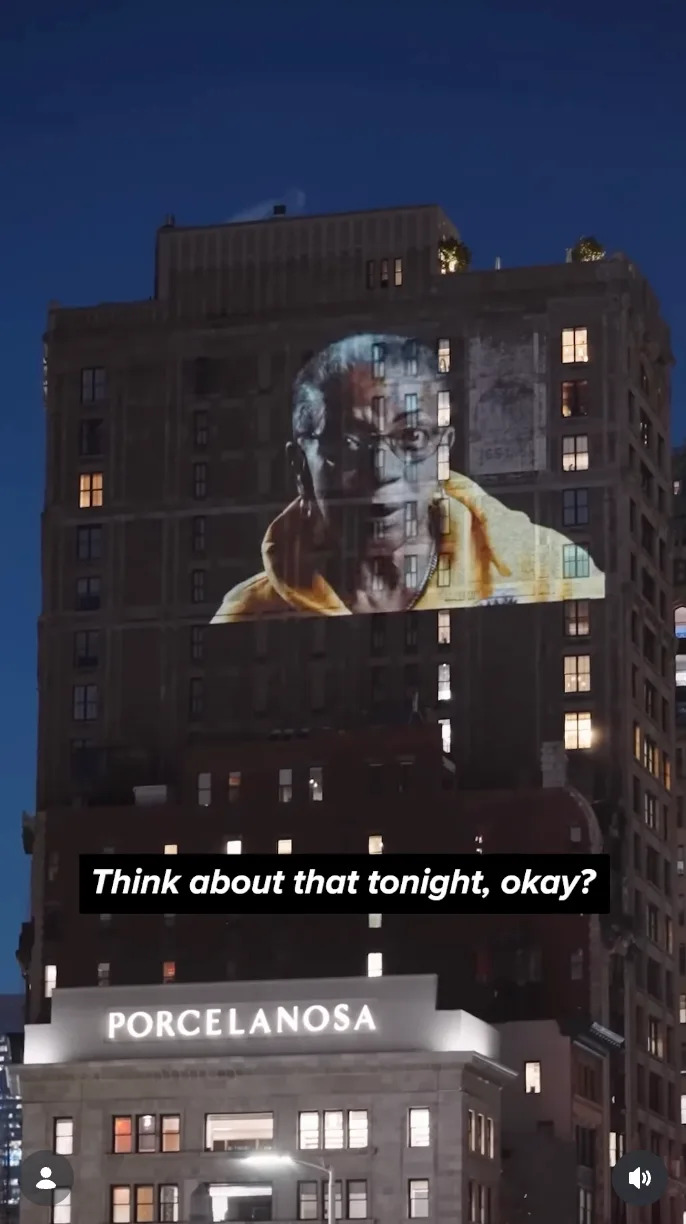 A building displays a large projection of a person speaking. Text reads: "Think about that tonight, okay?"