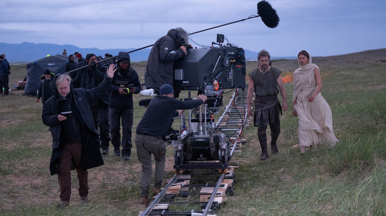 Director Christopher Nolan standing behind an IMAX camera across from Matt Damon as Odysseus and Zendaya as Athena on the set of The Odyssey