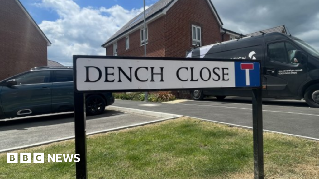 Swindon streets named after town’s role in James Bond film The Dench Close street sign fixed into the grass kerb side as you enter Dench Close with a van, a car and red-brick houses in the background.