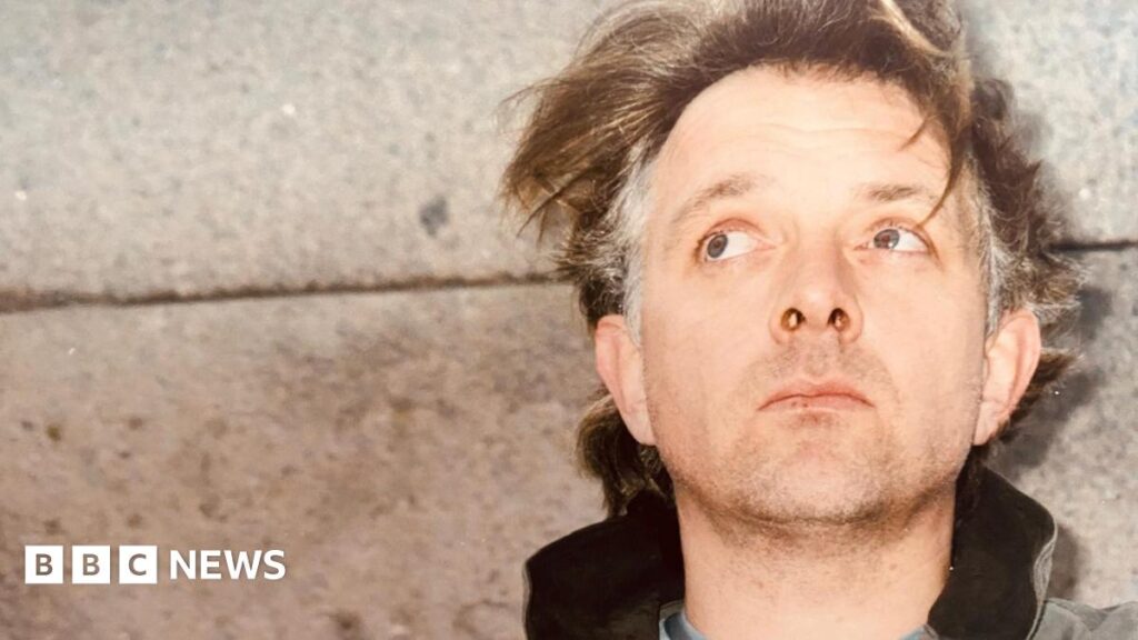 Droitwich Rik Mayall festival to show previously unseen material Comedian and actor Rik Mayall, standing with his back against a concrete wall. His hair, mid-brown with grey patches on the sides, is unkempt and he has a five o'clock shadow. He is looking up and behind the camera.
