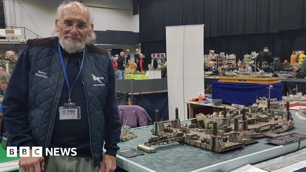 A man in his 80s dressed in navy stands beside a model of Mulberry Harbour