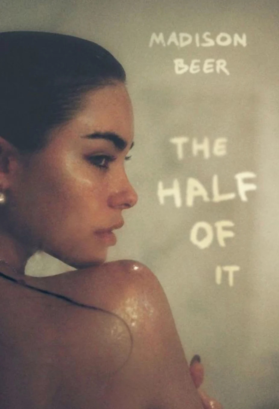 Cover of "The Half of It" by Madison Beer, featuring a close-up of a woman's face turned sideways, with wet skin and pearl earring
