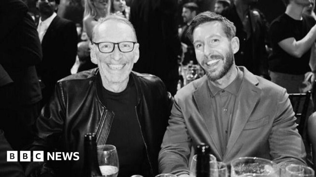 A black and white photo of DJ Calvin Harris in a suit with a T-shirt underneath alongside Mike Pickering in a leather jacket with dark glasses and grey receding hair