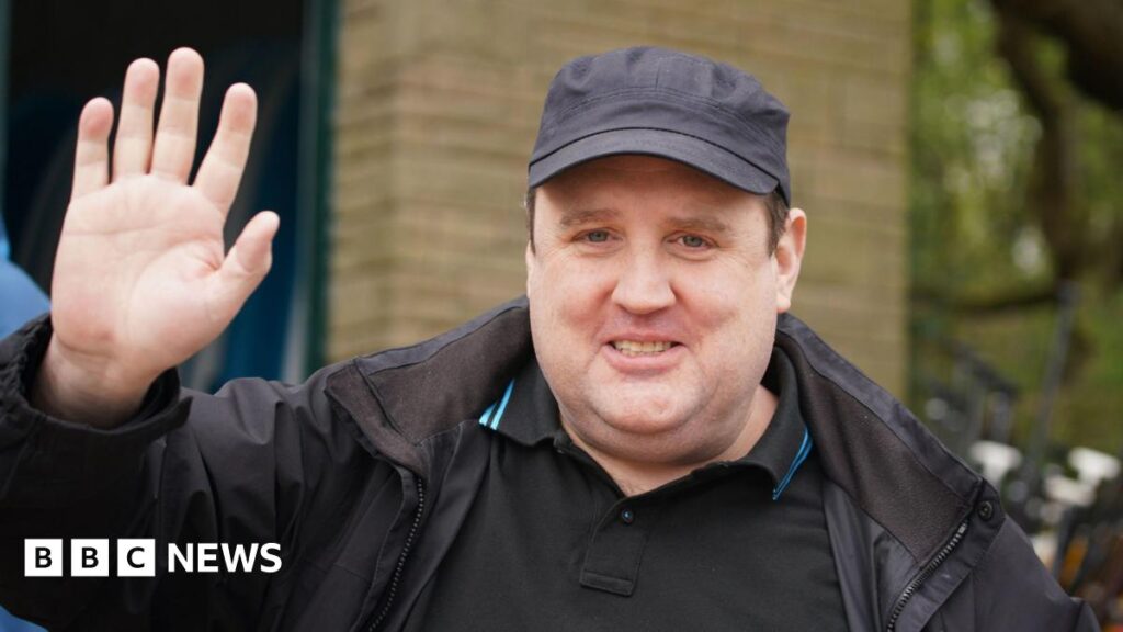 Peter Kay wears a cap and looks towards the camera