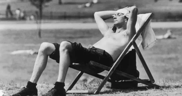 A man sunbathes in a deckchair in Kensington Gardens topless with a knotted handkerchief protecting his head from the sunshine