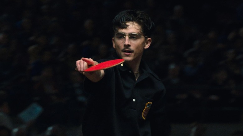 Marty holding a ping pong paddle and pointing in Marty Supreme
