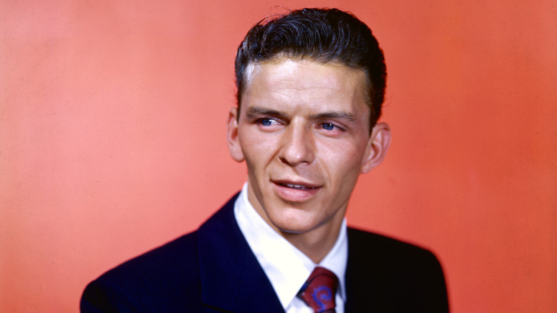 Frank Sinatra wears a dark blue suit against a red background in a studio portrait photograph, c. 1945.