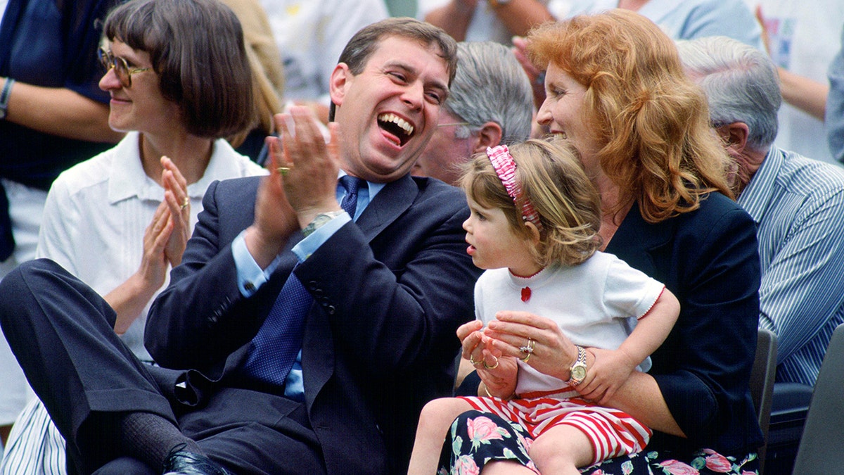 Prince Andrew and Sarah, Duchess of York, sitting laughing with Princess Eugenie on her lap at a sports day event