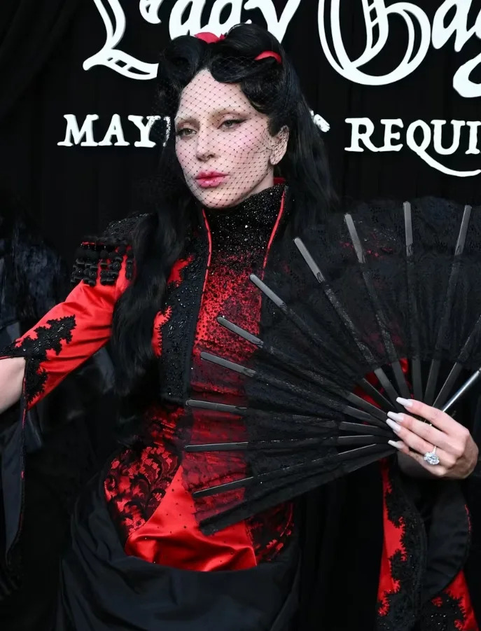 Lady Gaga's outfit combines red satin, black lace details, and dramatic accessories for a bold fashion moment.