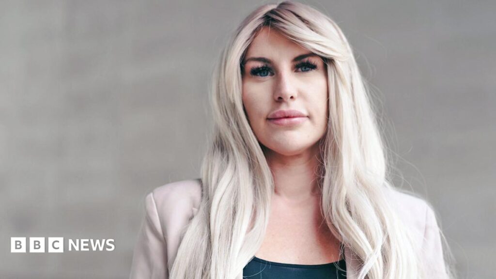 OnlyFans ‘agents’ exploit creators while taking half their earnings, BBC finds A head and shoulders portrait of Rebecca, standing against a light stone background. She has long blonde wavey hair and wears a black top with a light pink jacket. She looks pensively into the camera.