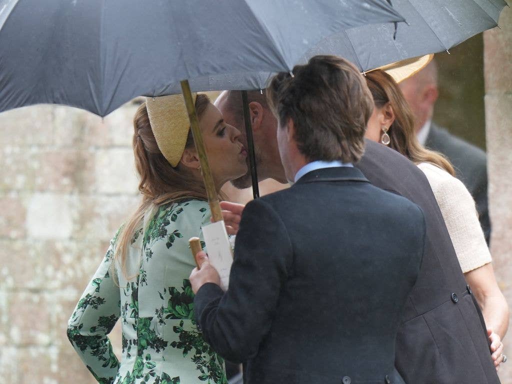 Prince William kissing Princess Beatrice on the cheek underneath an umbrella