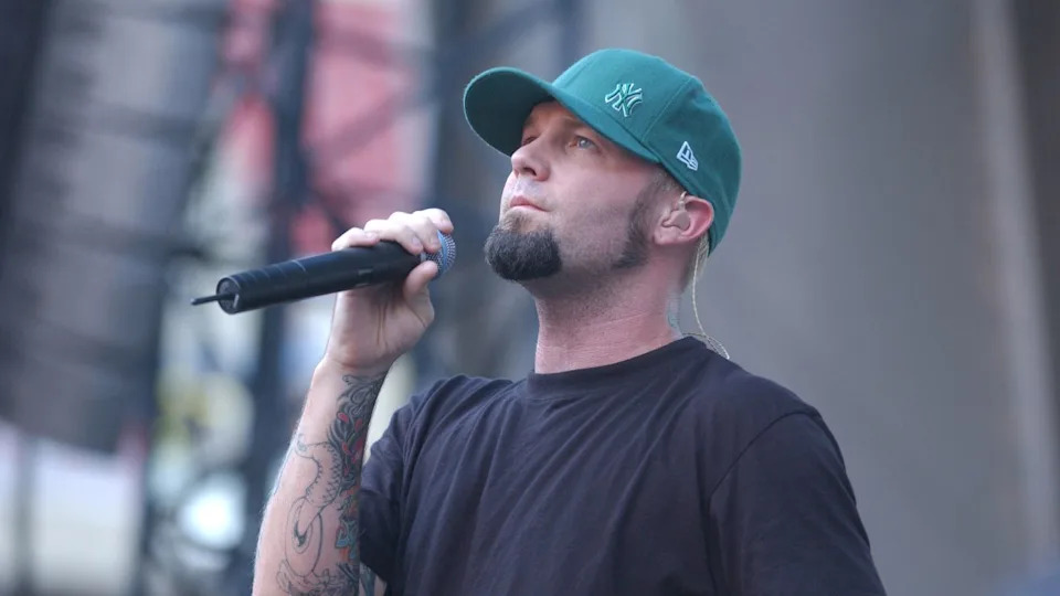 Fred Durst looking solemn on stage in a green cap.