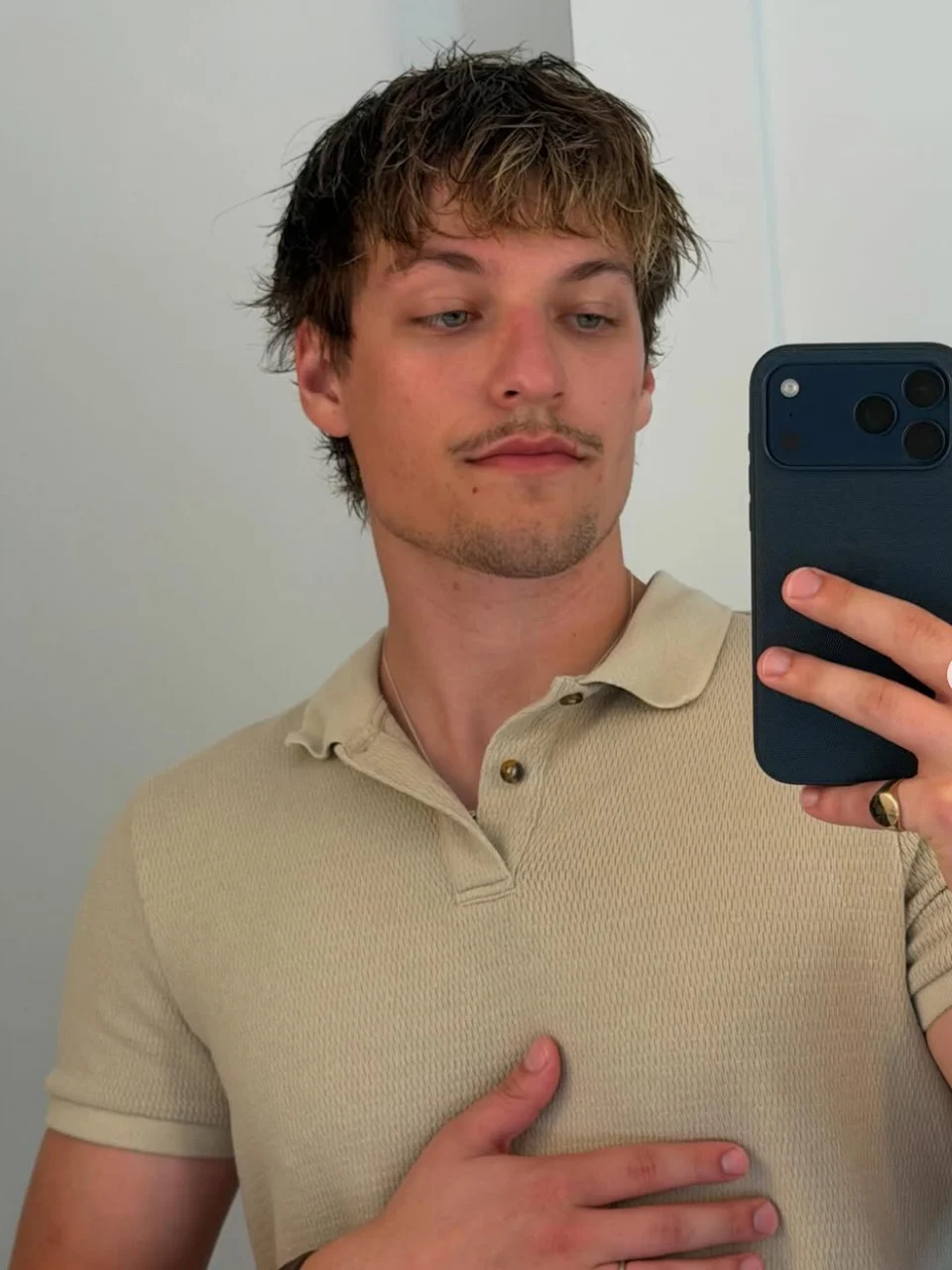 Person taking a mirror selfie, wearing a casual short-sleeve polo shirt, holding a phone with the other hand