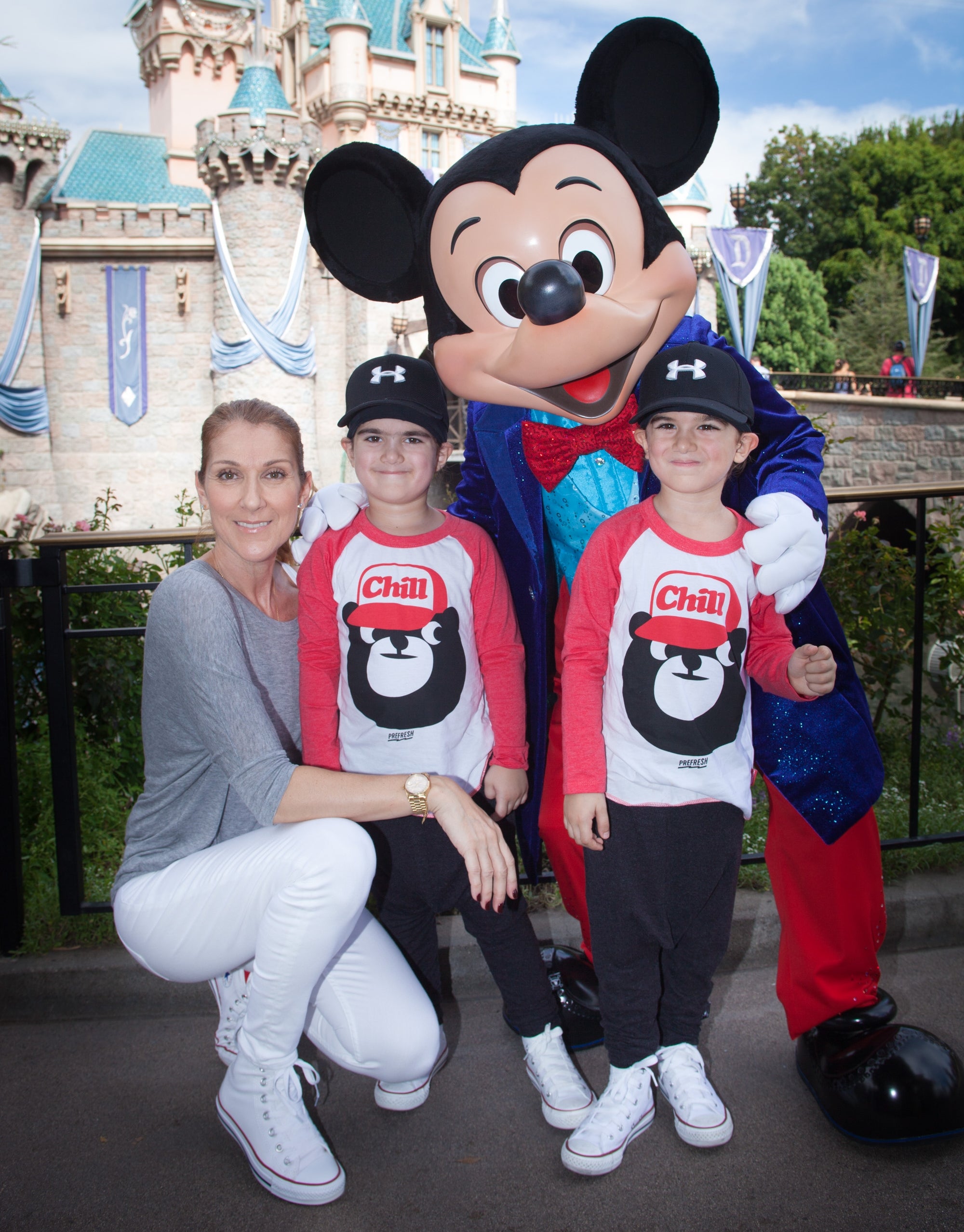 Person with two children posing with a Mickey Mouse mascot at a theme park. They are all smiling