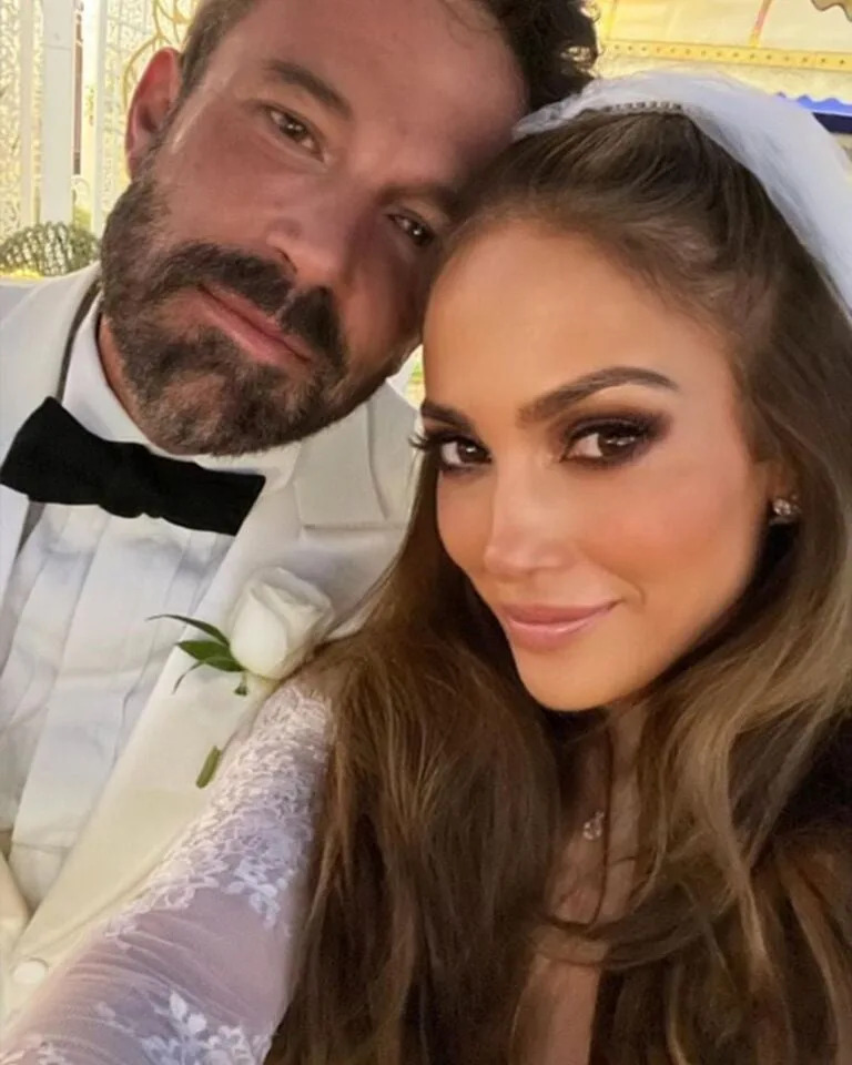 Jennifer and Ben pose closely, smiling, in wedding outfits