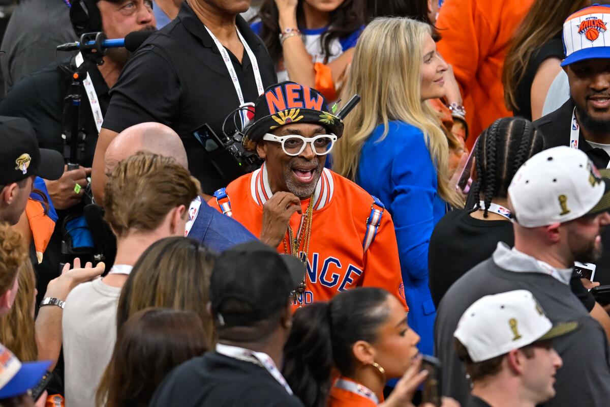 Spike Lee, dressed in Knicks gear, smiles as he stands in a crowd of fans