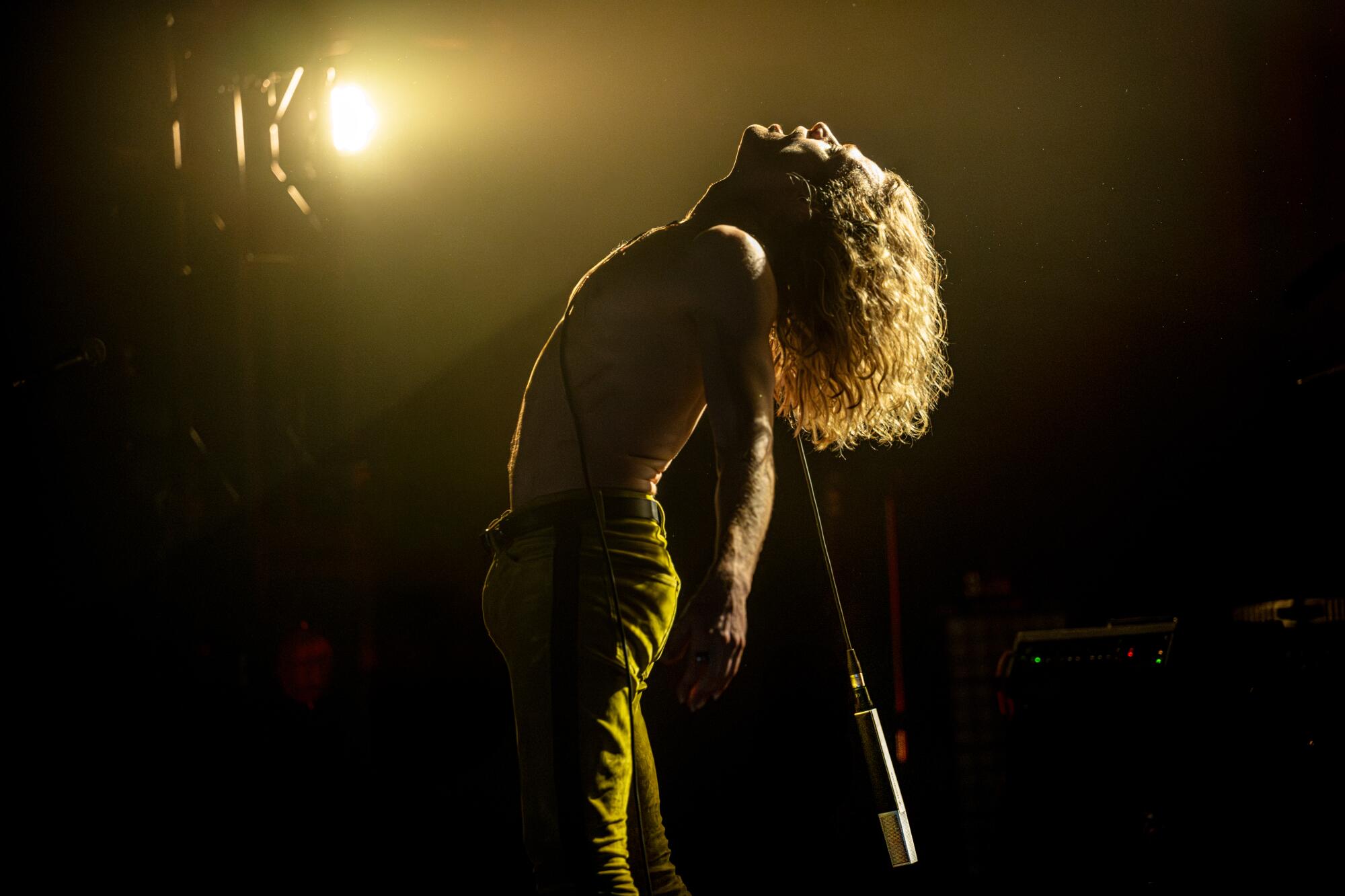 A long-haired rock star on stage arches his back and looks skyward