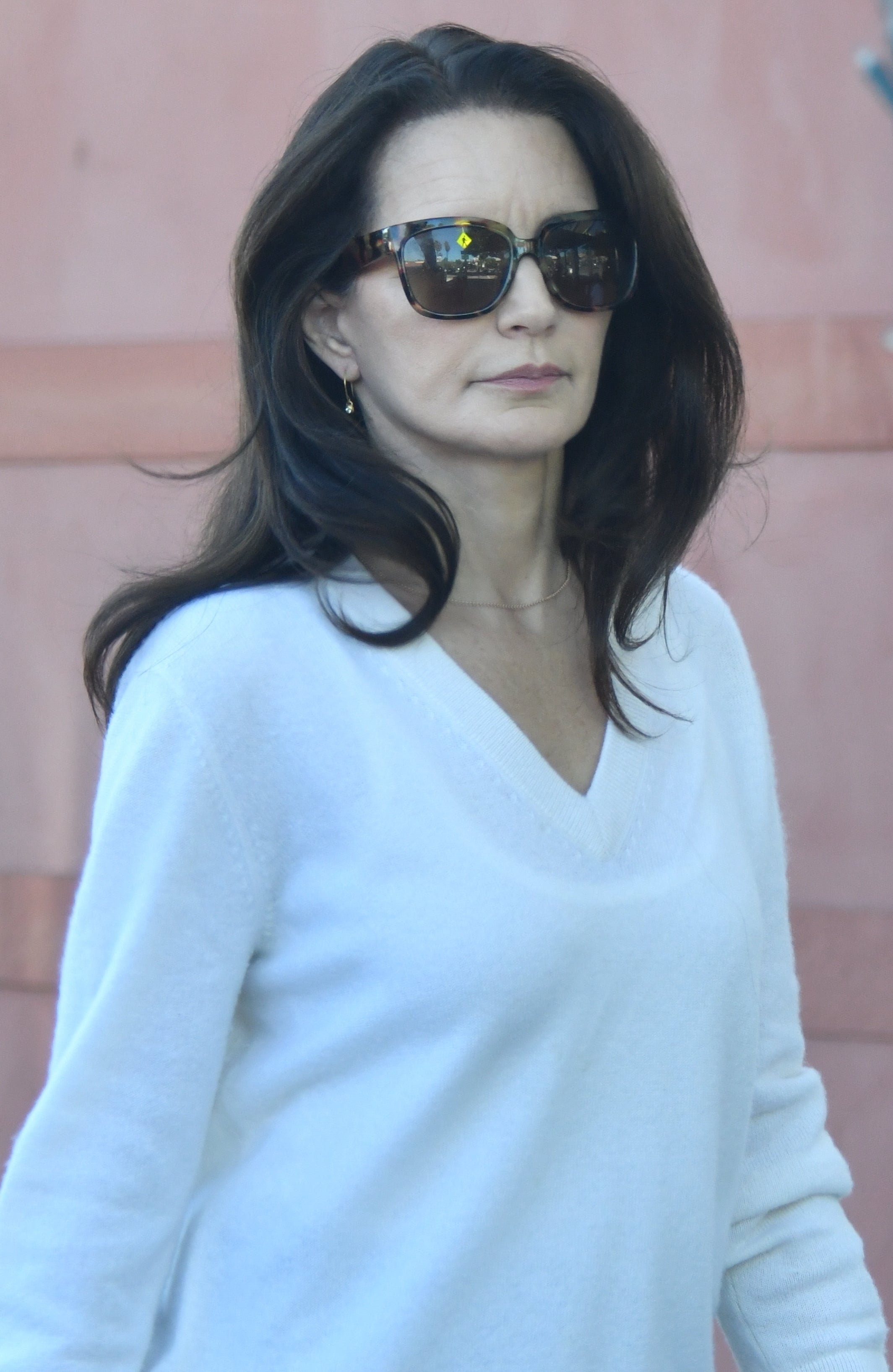 Person wearing a white sweater and sunglasses, walking outdoors with a neutral expression