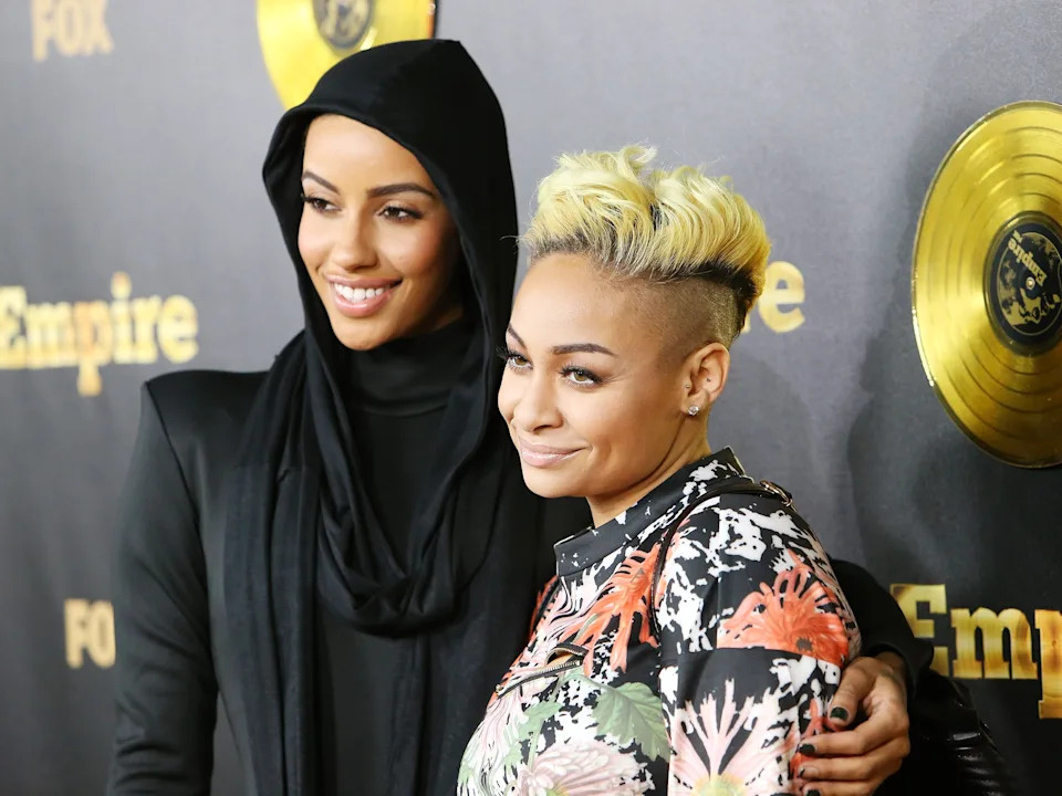 Two people posed at a "Empire" event. One is wearing a hooded jacket, and the other has a floral-patterned top with a stylish undercut