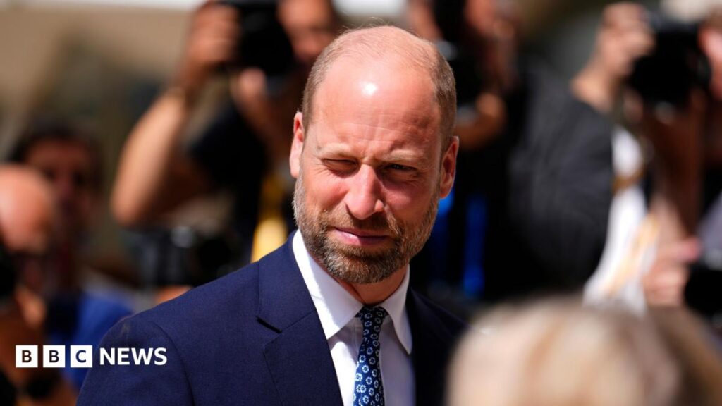 Prince William wears a navy blue suit and tie as he squints in the sunshine