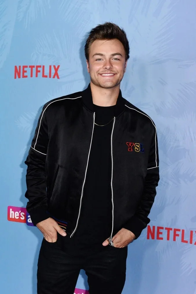 A person smiling at a Netflix event, wearing a casual black jacket over a t-shirt