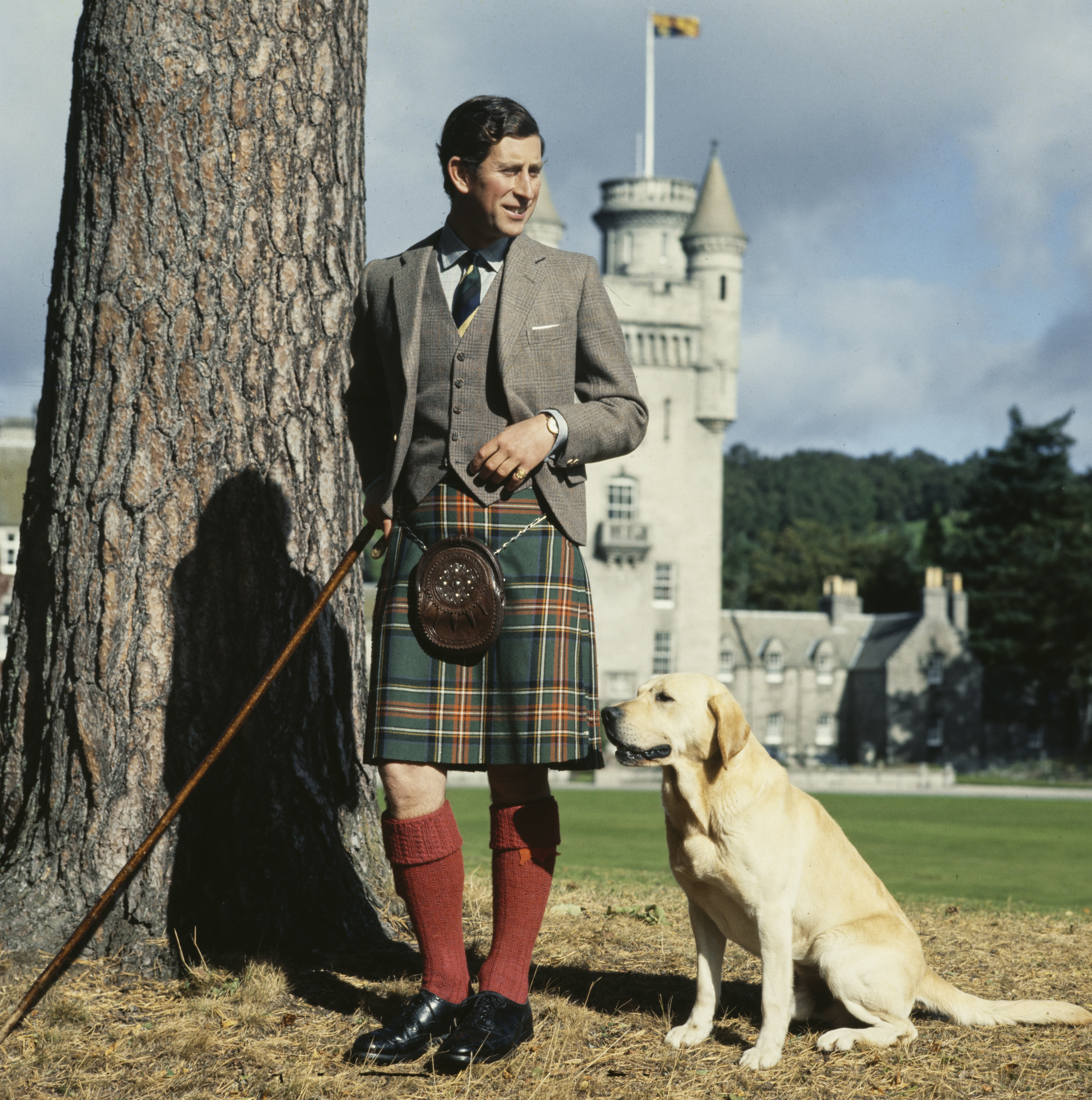 Prince Charles wearing a kilt standing with his dog in front of Balmoral
