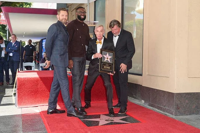 Four people pose with a Hollywood Walk of Fame star plaque. One holds the plaque, smiling, as the others stand nearby on the red carpet