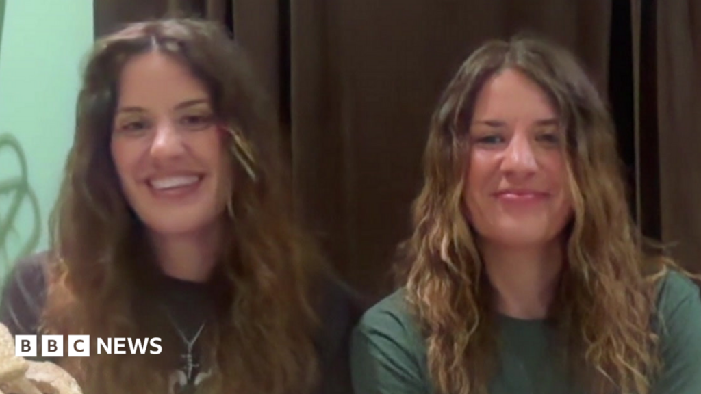 Georgia and Melissa Laurie, both sat in front of a webcam, smiling for the camera as they speak during an interview with BBC Breakfast. They both have long, brown or brown/blonde hair. Georgia is wearing a black T-shirt and Melissa a green T-shirt.