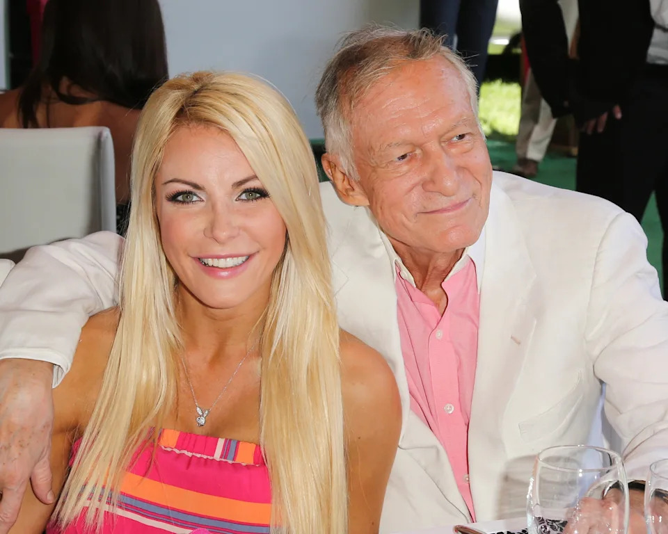 Two smiling people seated together, one with long hair in a striped dress, the other in a white jacket and pink shirt