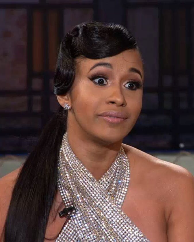 Person with long hair and glittering dress, sitting with a raised eyebrow expression.