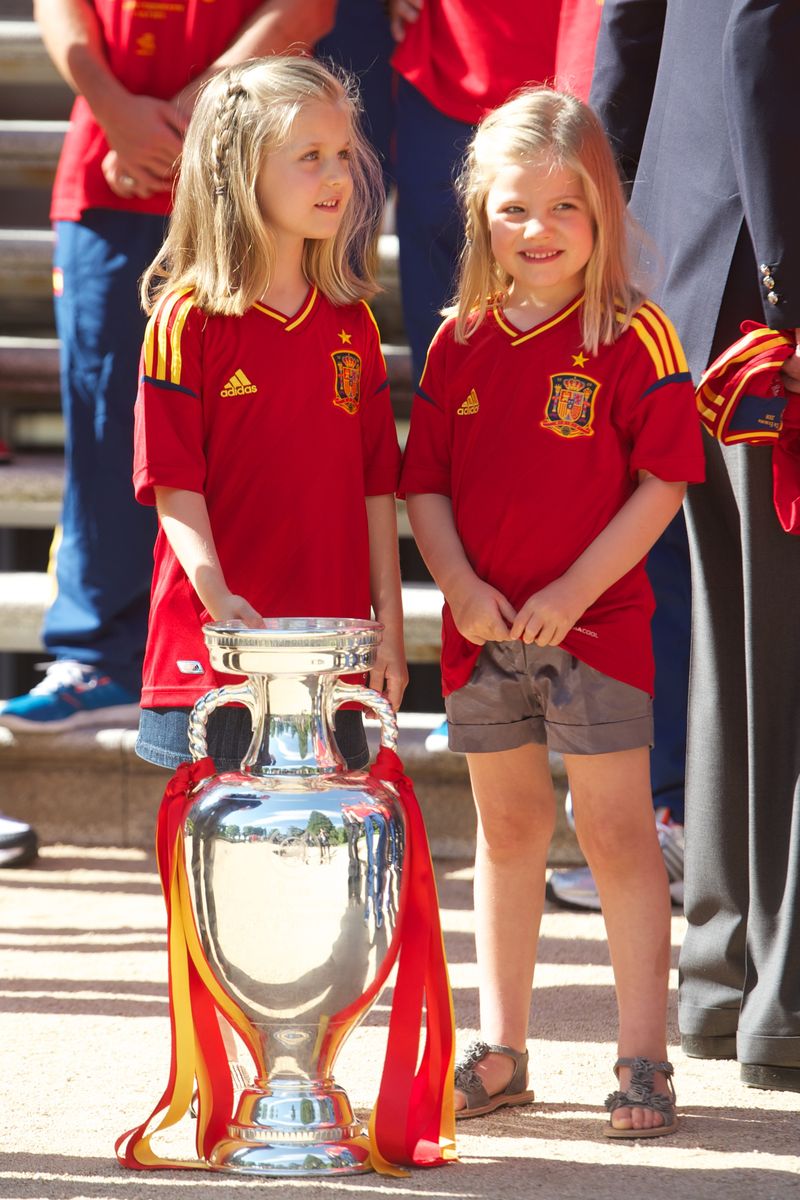 MADRID, SPAIN - JULY 02:  Princess Leonor of Spain (L) and Princess Sofia of Spain stand next to the UEFA EURO 2012 trophy as King Juan Carlos I of Spain receives players of Spain's victorious national football team at Zarzuela Palace on July 2, 2012 in Madrid, Spain.  (Photo by Pool/Getty Images)