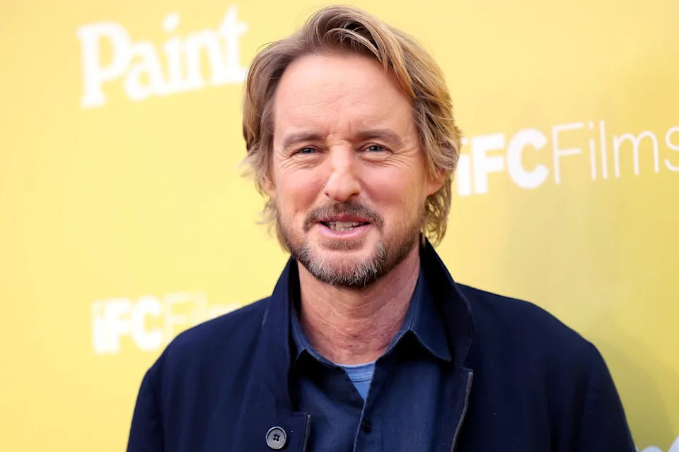 A man with medium-length hair and facial hair is on a press line in a casual jacket and shirt. The backdrop has small text reading “Paint” and “IFC Films.”