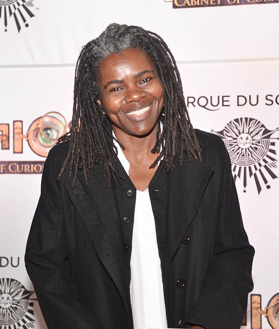 Person smiling at an event, wearing a black coat over a white shirt, in front of a