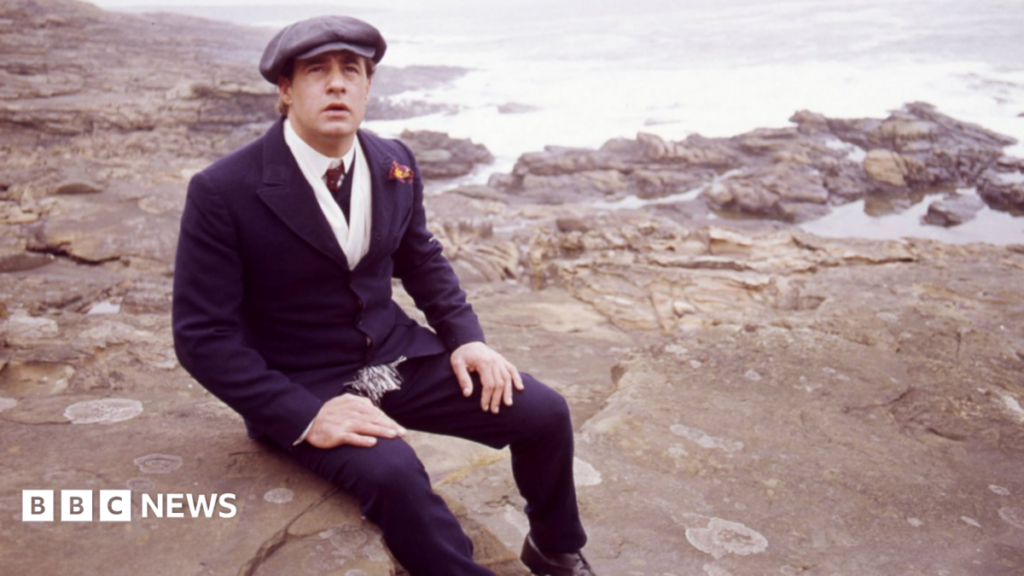 Boon and Coronation Street actor David Daker dies David appearing in Centre Play: God Bless Thee Jacky Maddison - Play by Tom Hadaway. Picture shows David Daker as Jacky Maddison. He is sat on rocks on a beach with a hat on.