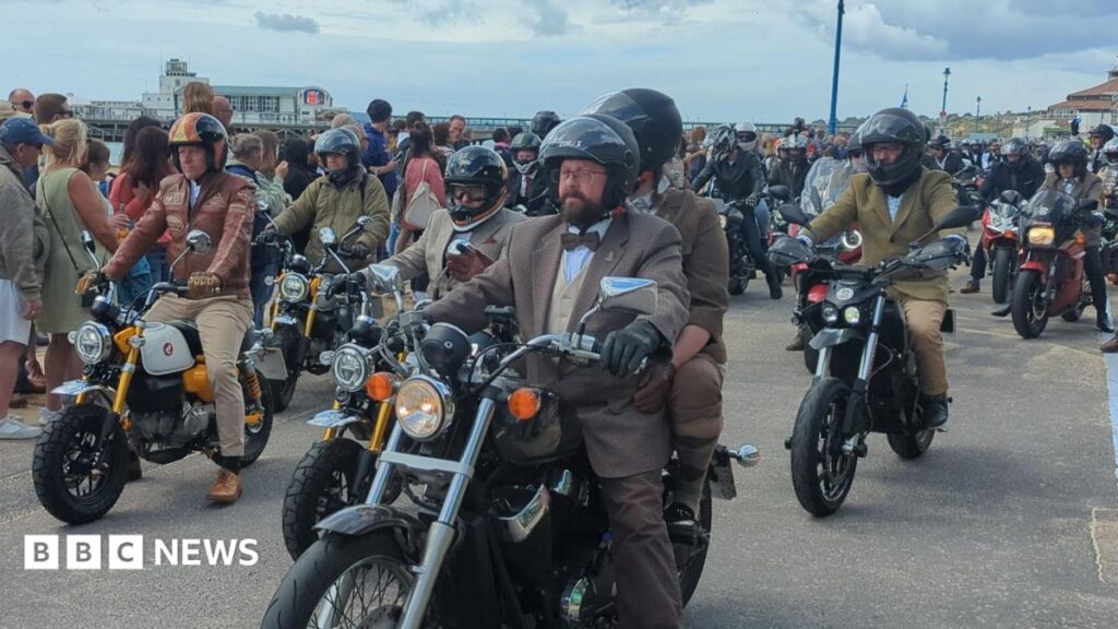 Charity motorcycle ride in Dorset ranks second in world for donations A group of motorbike riders are heading past the camera. They are all wearing similar brown suits. The closest rider to us has a brown bow tie, a beard, and is wearing glasses.