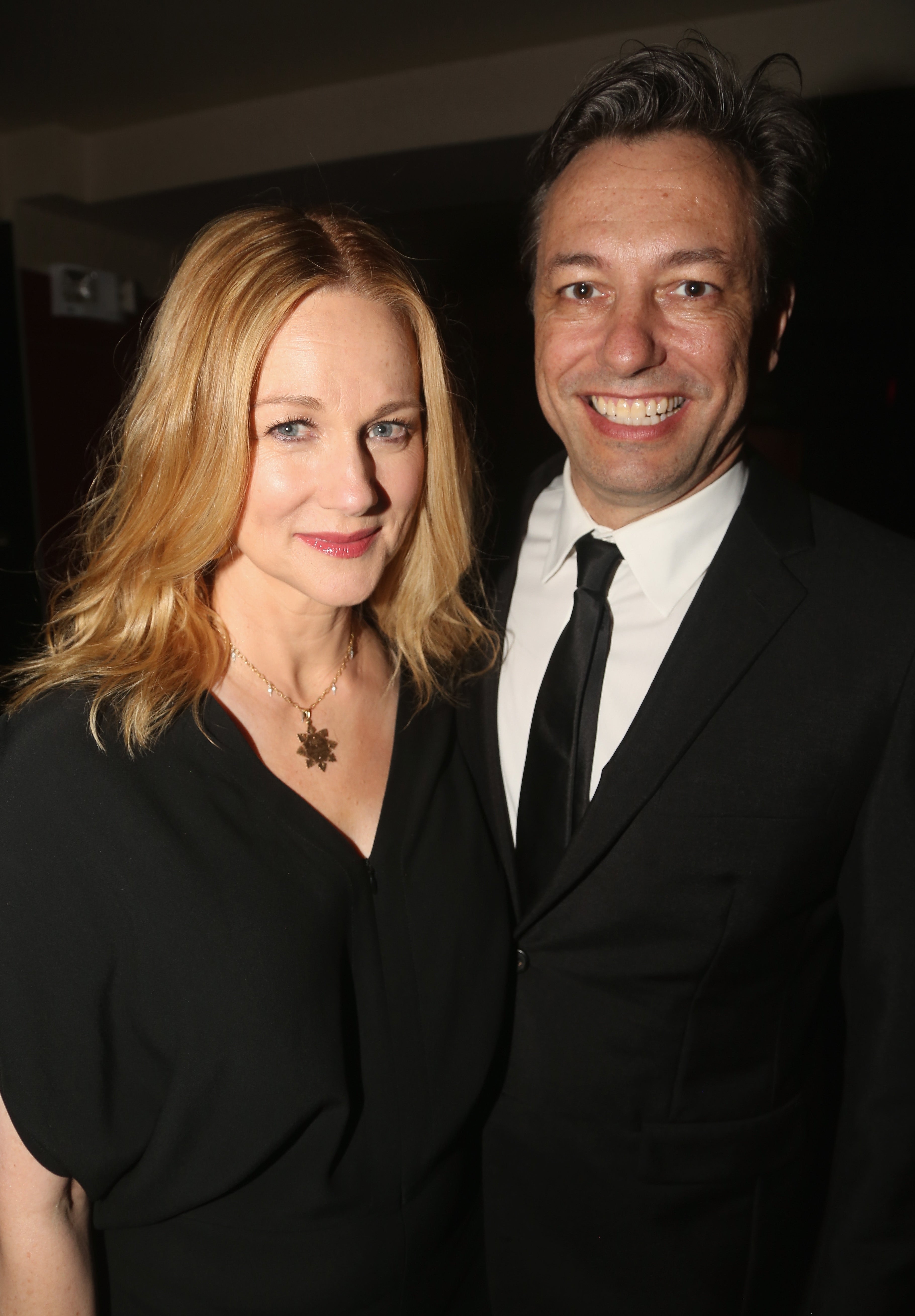 A woman in a black dress and a man in a suit and tie smile for the camera, standing together at an event