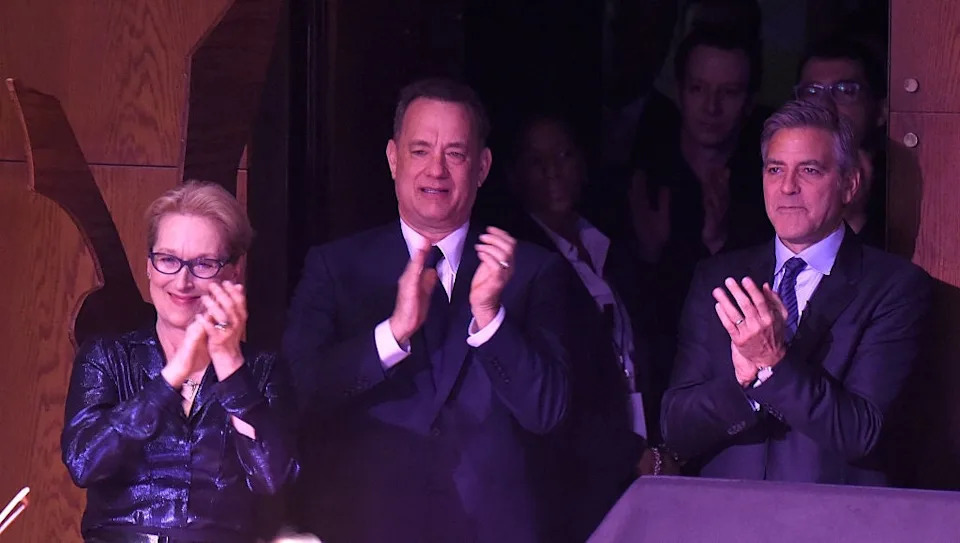 Three people stand applauding at an event, dressed in formal attire