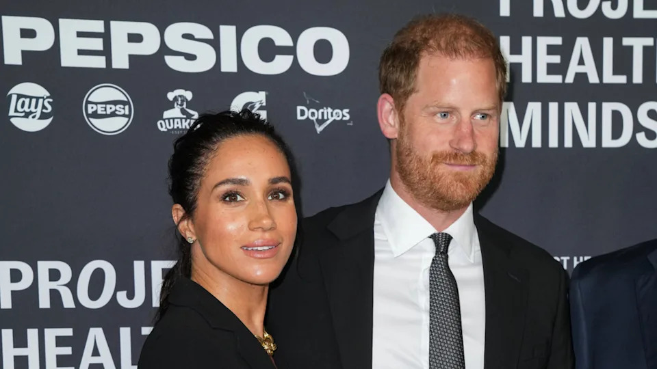 Prince Harry and Meghan Markle at an event, standing together in formal attire against a PepsiCo backdrop.