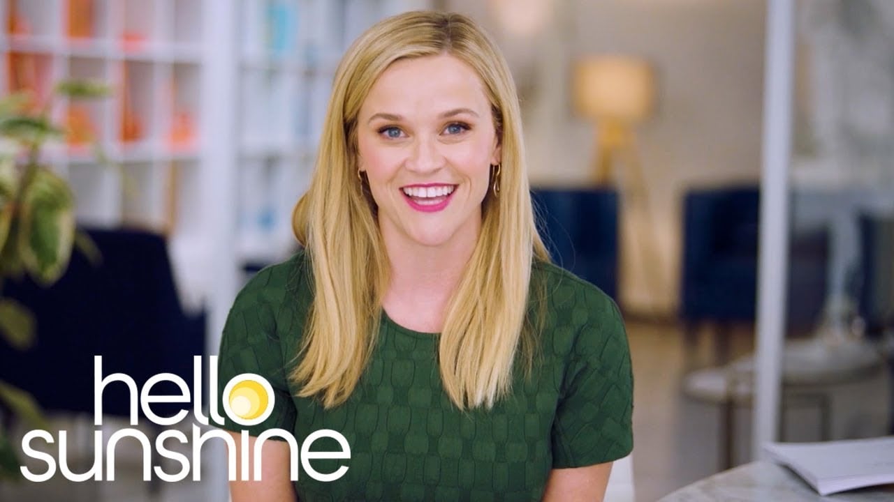 A smiling blonde woman in a green top sits indoors with shelves and a lamp in the background. The words "hello sunshine" are displayed in white and yellow text at the bottom left of the image.