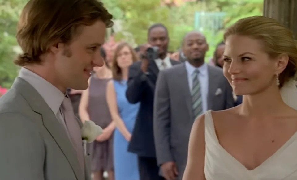 Scene from House: A couple in wedding attire exchange smiles. Guests in formal wear observe the moment outdoors