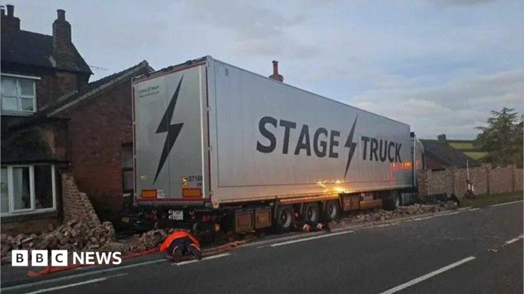 ‘Rock band’s truck’ crashes into house on way to Download A grey lorry with the word "Stage Truck" on the side, which has left the road and brick rubble can be seen around it.