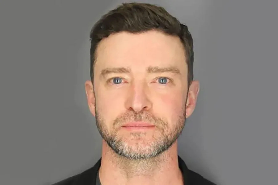 Justin Timberlake with short hair and facial stubble, dressed in a top, looks directly at the camera against a plain background