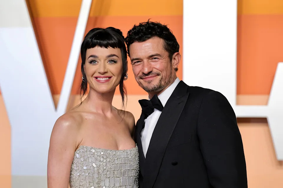 A woman in an elegant strapless dress and a man in a classic tuxedo pose together, smiling at a formal event