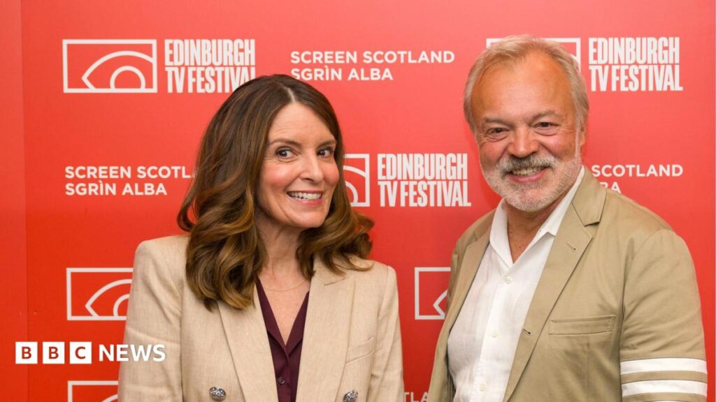 American comedian, writer and producer Tina Fey with presenter Graham Norton at the Edinburgh TV Festival, in the Edinburgh International Conference Centre. They stand in front of a red and white Edinburgh TV Festival backdrop.