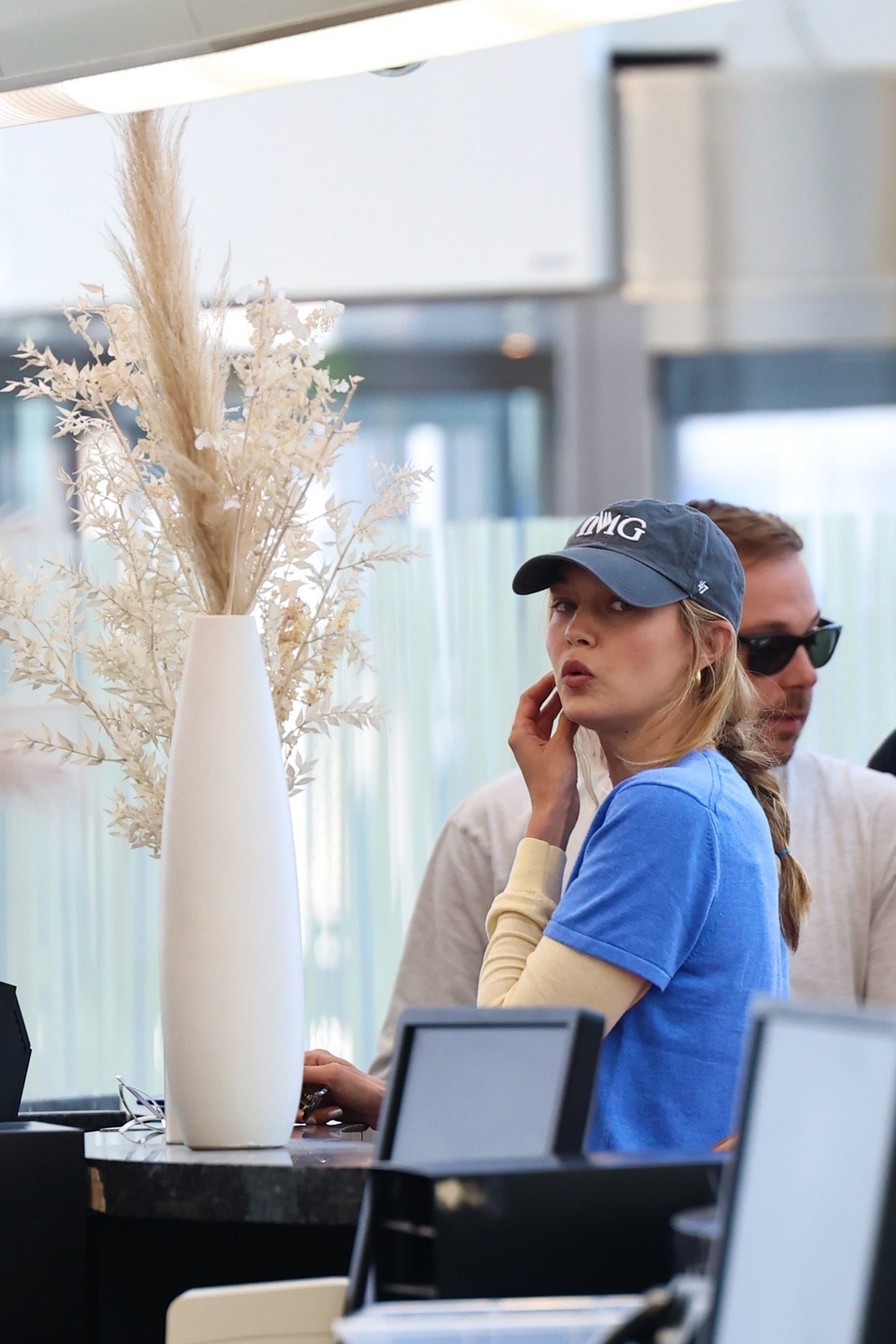Gigi Hadid at the airport wearing a blue T-shirt, white pants, yellow loafers, and a black baseball cap