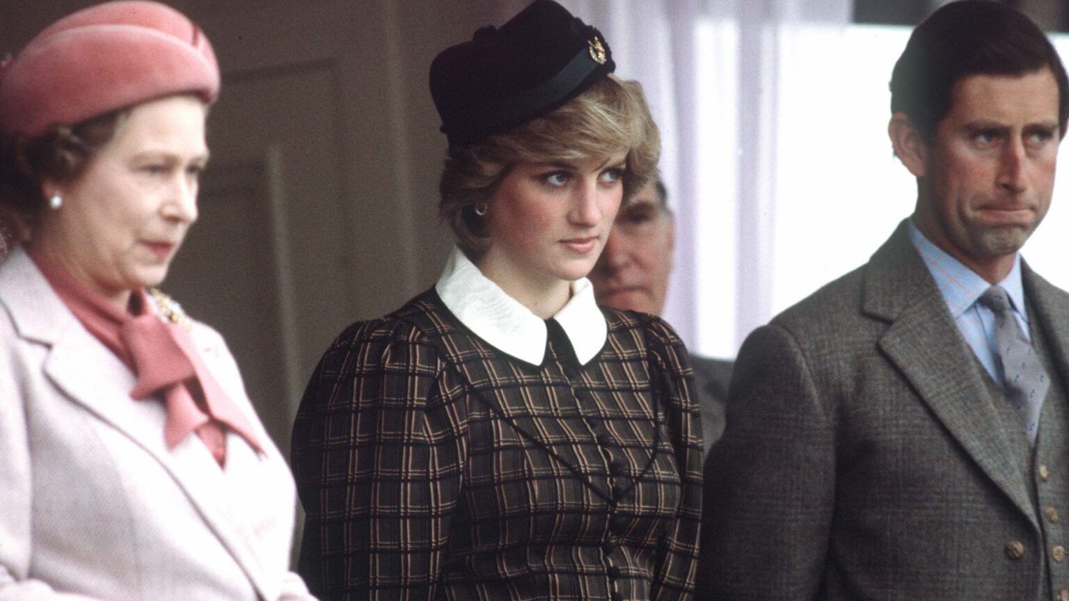 Princess Diana wears a tartan dress with a white collar and stands between Queen Elizabeth II, who wears a light pink coat, and King Charles