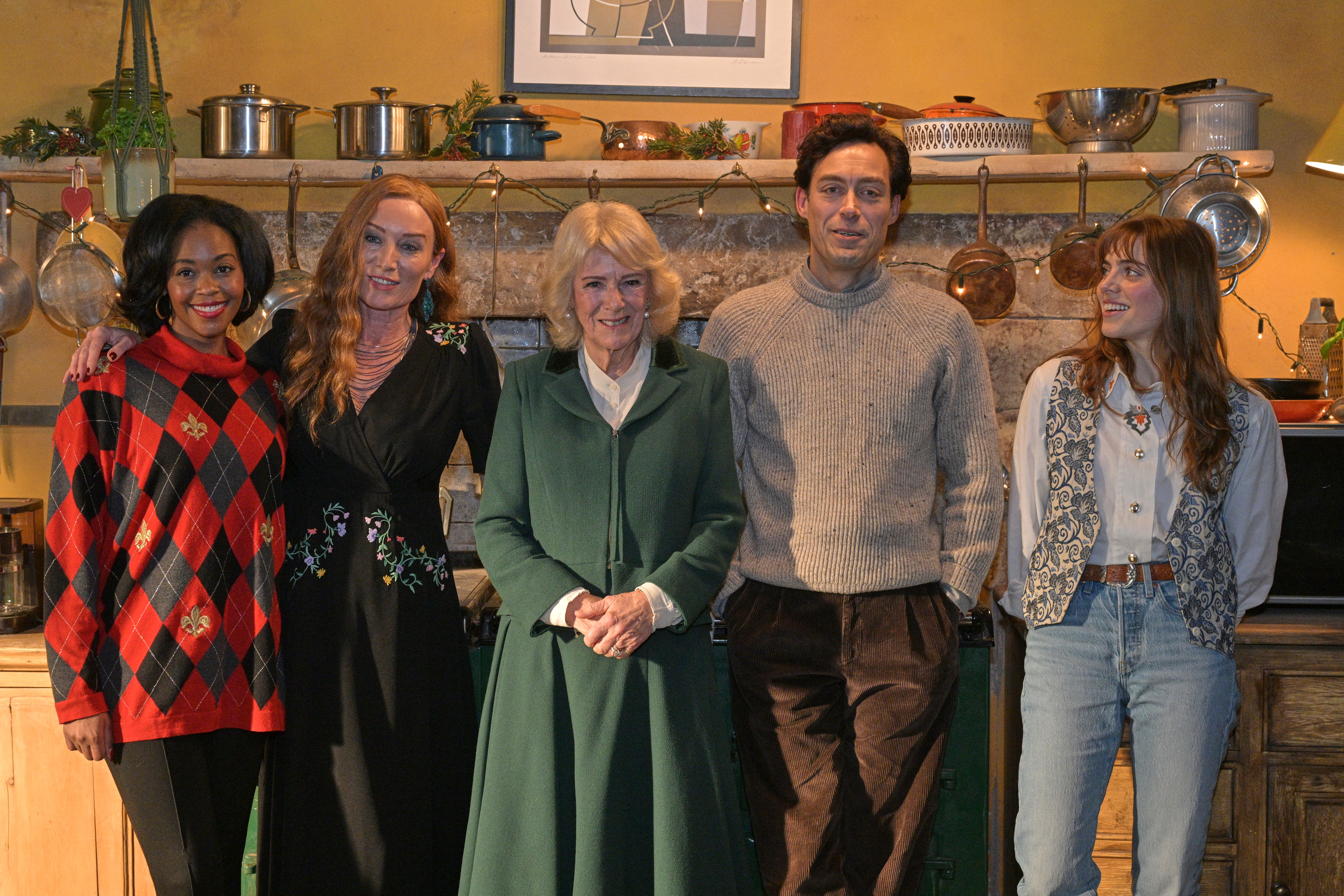 Queen Camilla and the cast of Rivals posing in front of a fireplace