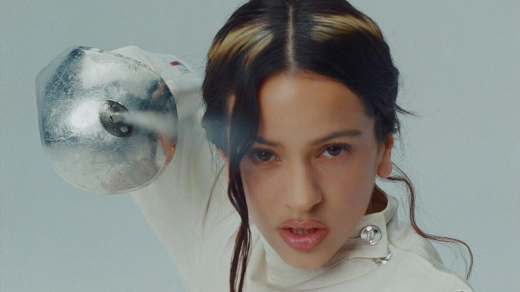 Rosalía postpones Miami shows due to family emergency close-up photo of singer Rosalía with a halo-shaped highlight in her hair, pointing a sword into the camera