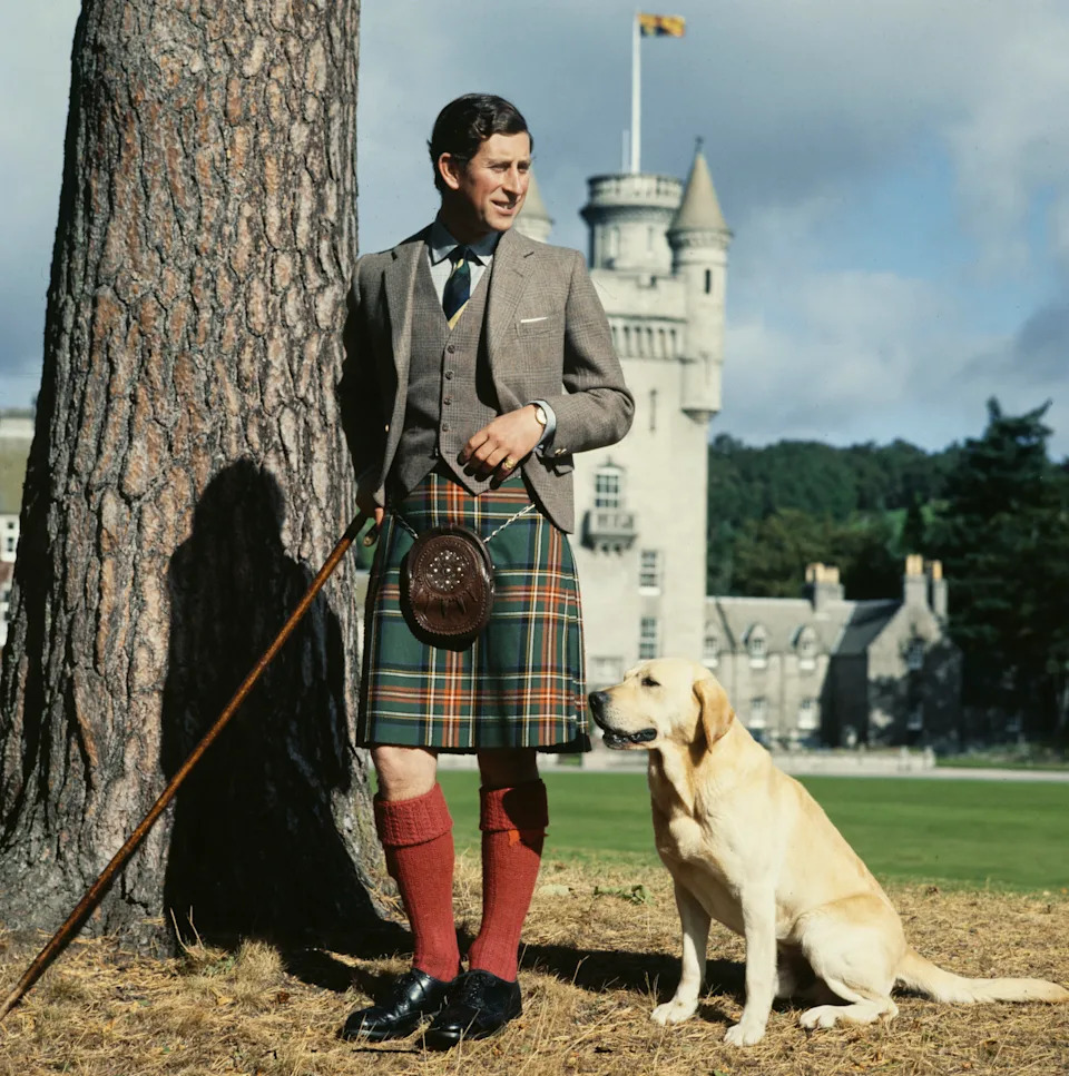 Prince Charles wearing a kilt standing with his dog in front of Balmoral