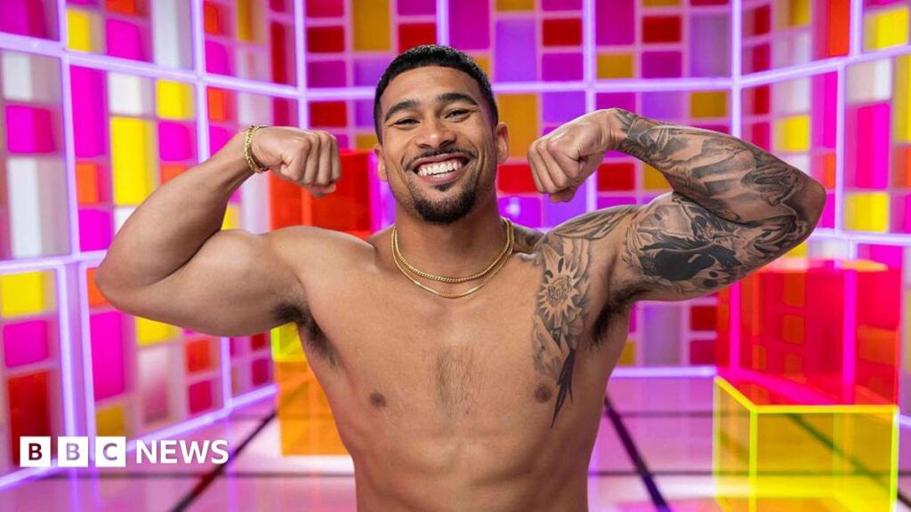 Police Officer turned Love Island US contestant faces backlash Sean Reifel seen posing shirtless while flexing his muscles in front of a colorful backdrop as part of a Love Island USA photoshoot.